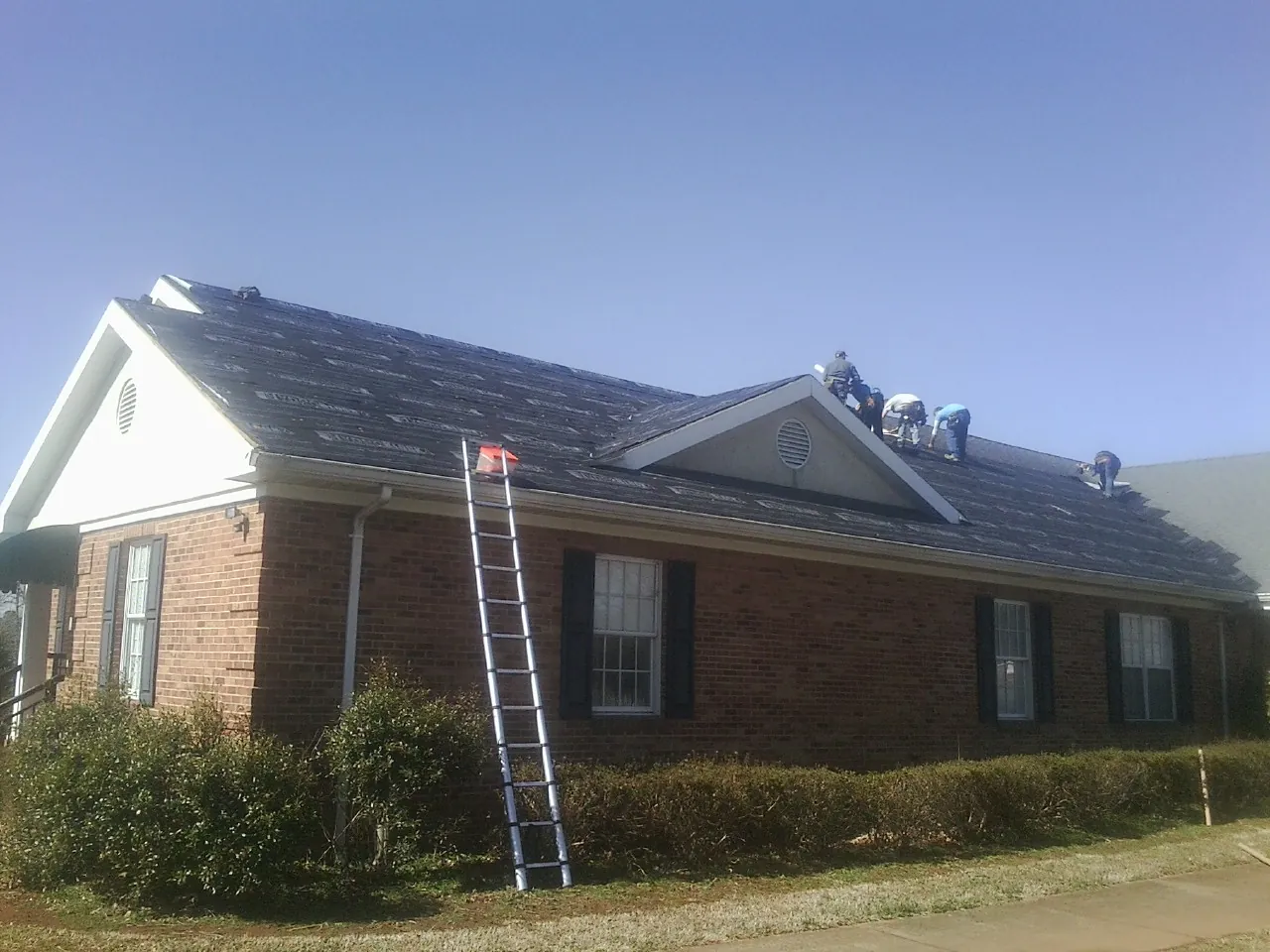 Crew tearing shingles off a brick ranch roof with a ladder set — Metal Roof Repair work by our crew in Lanham