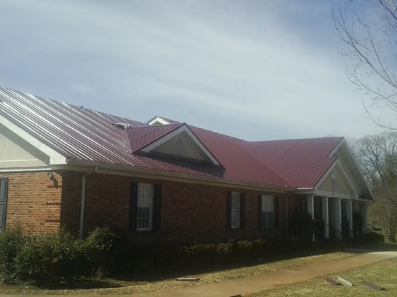 Red metal roof with gabled entries on a long brick building, from a Hail Damage Roof Repair job in Lanham