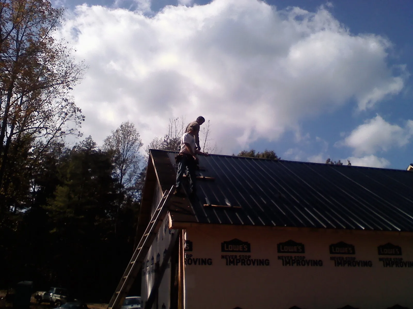 Roofer fastening dark metal panels high against a cloudy sky, from a Roof Inspection job in Lanham