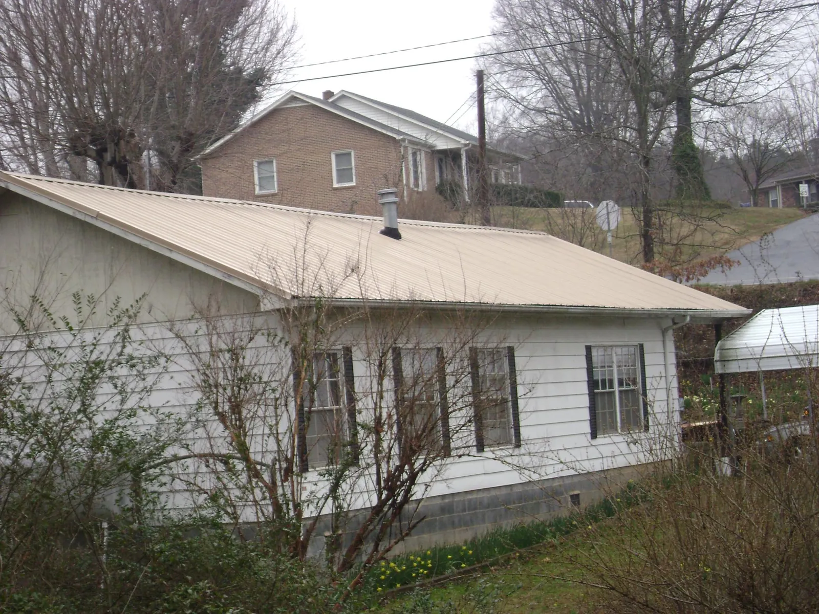 Tan metal roof on a white sided house set into a hillside — Commercial Roofing by Roofing Brothers in Lanham